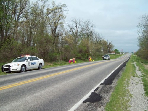 inmates with trash bags and two sheriff vehicles parked on side of road