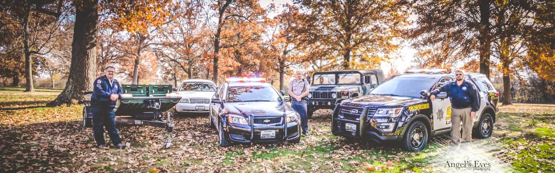 Assortment of LCSO vehicles including cars, suvs, humvee, and a boat.