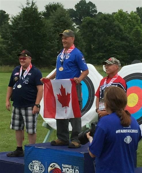 3 men standing on podium, one holding a Canadian flag